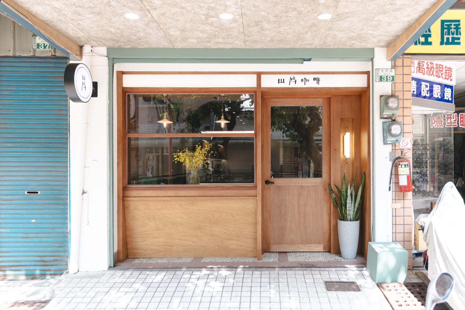 山鳩咖啡的店門口，木框玻璃門與旁邊的藍綠色鐵捲門